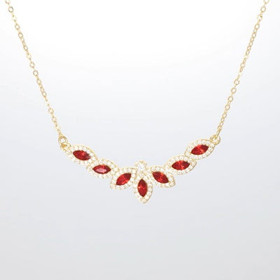 Halskette mit funkelndem Blütenanhänger aus roten Kristallen in goldfarbener Fassung.